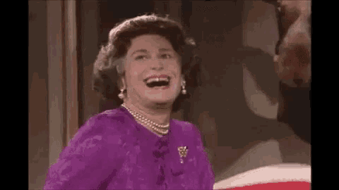queen elizabeth ii is wearing a purple dress and pearls and laughing .