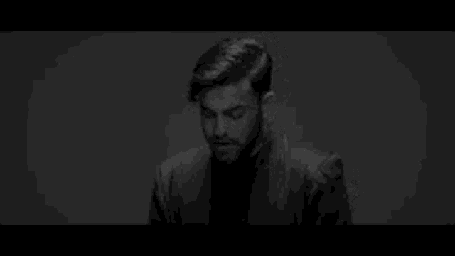 it is a black and white photo of a man with a beard looking down .