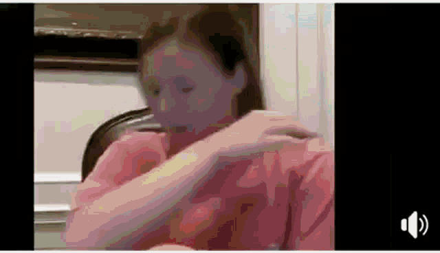 a woman in a pink shirt is sitting in a chair with her hand on her chest .