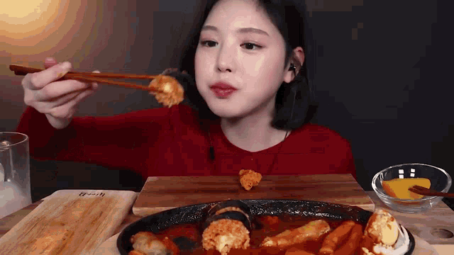 a woman in a red sweater is eating food with chopsticks .