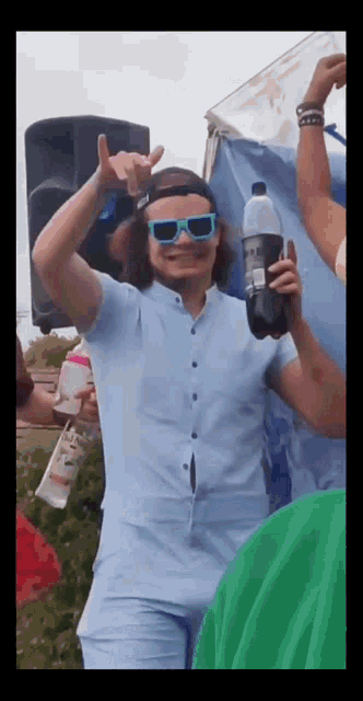 a man wearing sunglasses and a hat holds a bottle of soda