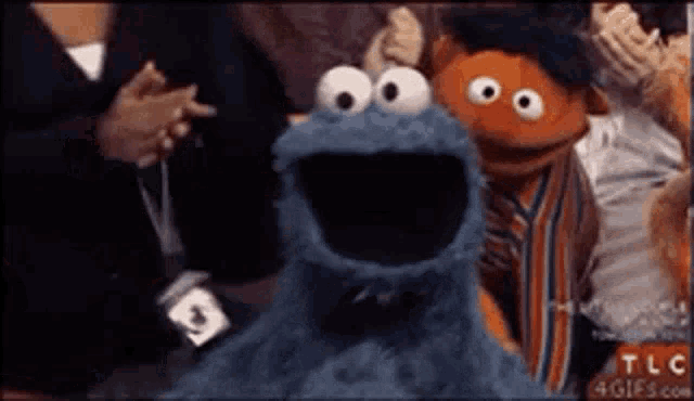 a cookie monster and ernie puppet are standing next to each other in a crowd .