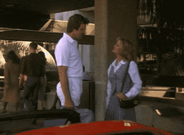 a man and a woman standing next to each other with a red car in the background
