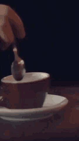 a person is stirring a cup of coffee with a fork .