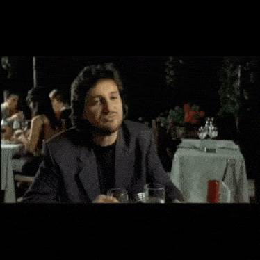 a man in a suit sits at a table with the words il contooo written above him