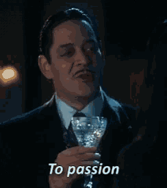 a man in a suit and tie is holding a martini glass and saying `` to passion '' .