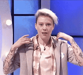 a woman with short hair and tattoos on her arms is standing in front of a blue background .