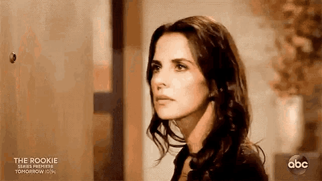 a woman is standing in front of a door looking at the camera with a serious look on her face .