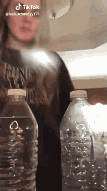 a woman is standing next to two empty water bottles with a tik tok watermark on the bottom