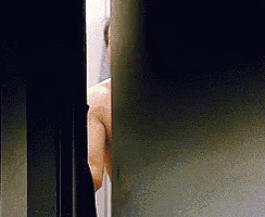 a man without a shirt is standing in a doorway looking out .