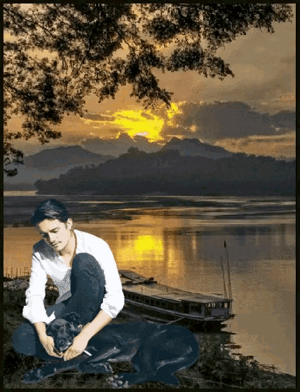 a man sits next to a black dog in front of a lake
