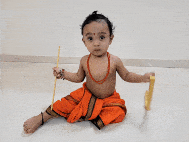 a baby in an orange outfit is holding a stick