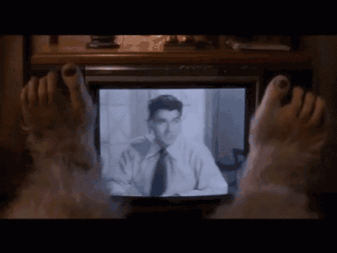 a person 's feet are laying on a television screen watching a man