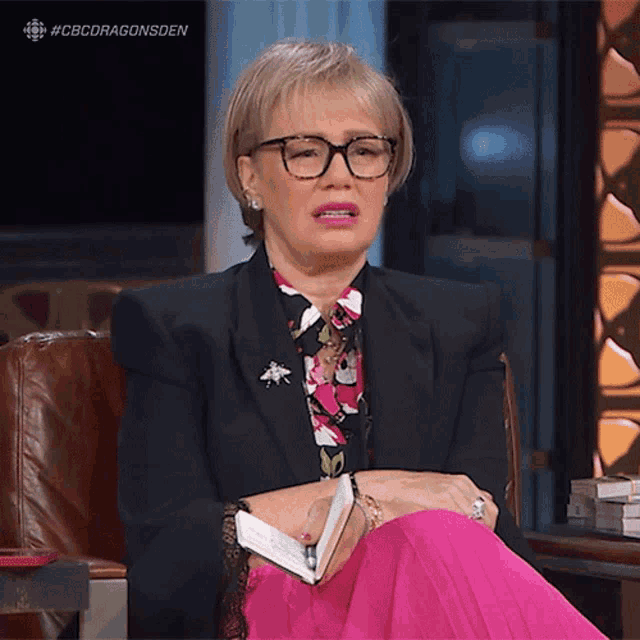 a woman wearing glasses and a black jacket is sitting in a chair with the hashtag #cbcdragonsden