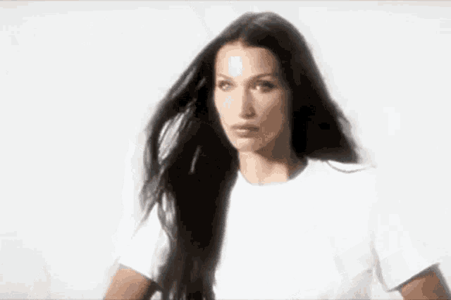 a woman with long black hair is wearing a white t-shirt and looking at the camera .