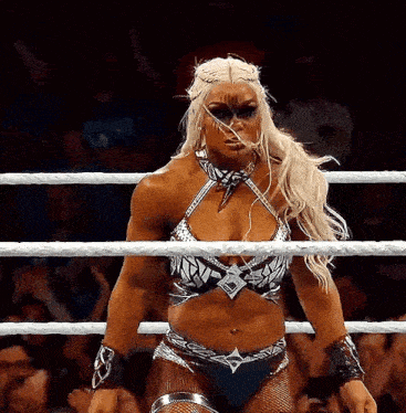 a female wrestler is standing in a wrestling ring with a crowd watching .