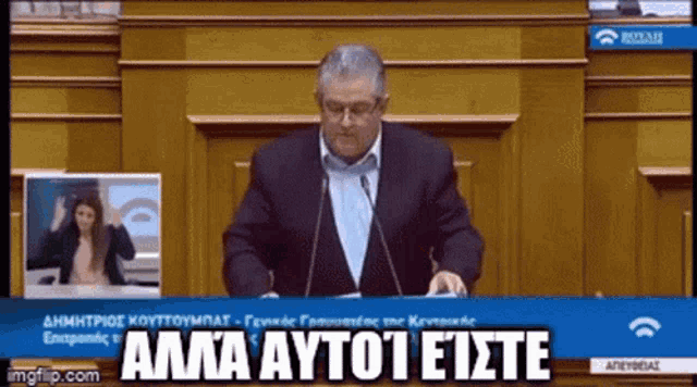 a man in a suit is giving a speech in front of a microphone with the words ama autoi eiste written on the screen