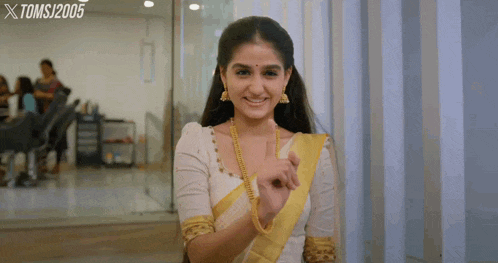 a woman in a white and yellow saree is smiling and giving a thumbs up sign