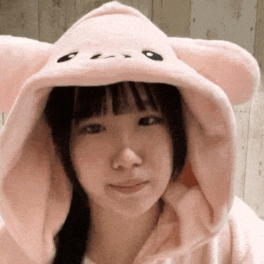 a young girl wearing a pink hoodie with ears and a face on it