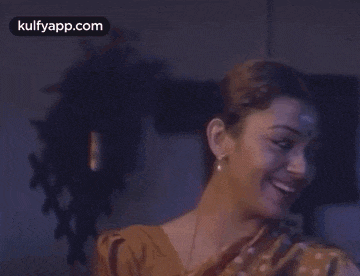 a woman is smiling and laughing in a dark room with a kulfyapp.com logo on the bottom right corner .