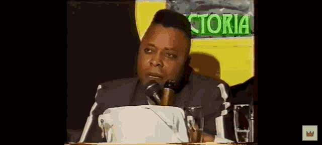 a man is speaking into a microphone in front of a sign that says ctoria
