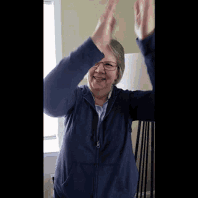 a woman wearing glasses and a blue hoodie is giving a high five