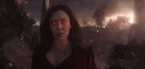 scarlet witch with red eyes is standing in front of a burning building .