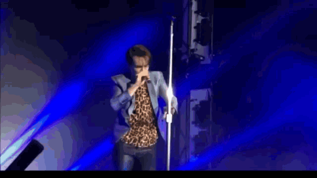 a man in a leopard print shirt is singing into a microphone while dancing on a stage .