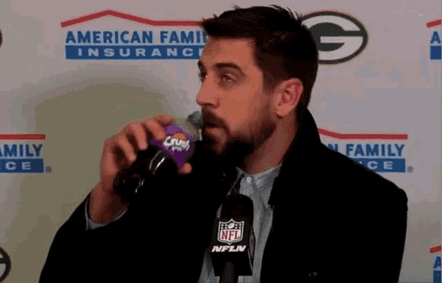 a man drinking from a crush bottle in front of an american family insurance banner