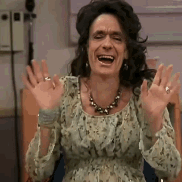 a woman in a floral dress and necklace is laughing with her hands in the air