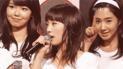 a woman singing into a microphone with tbc sbs written on the bottom right