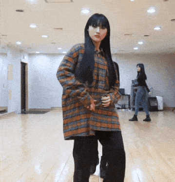a girl in a plaid shirt is dancing in a room
