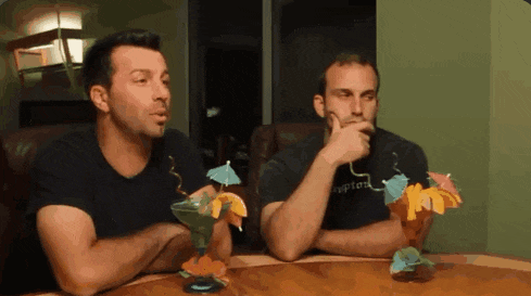 two men are sitting at a table with drinks and one has a shirt that says appleland