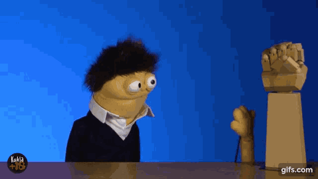a puppet is sitting at a table with a blue background and a gifs.com logo