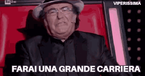 an older man wearing a hat and glasses is sitting in a red chair and says farai una grande carriera .