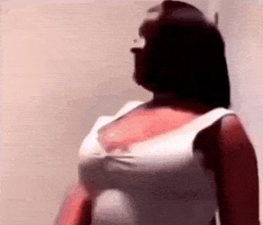 a woman in a white tank top is standing in front of a wall and looking at the camera .