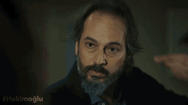 a man with a beard has the hashtag #hekimoglu written below him