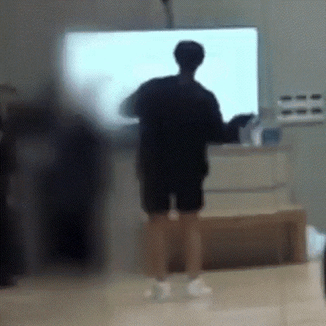 a blurry picture of a person standing in front of a large screen tv .