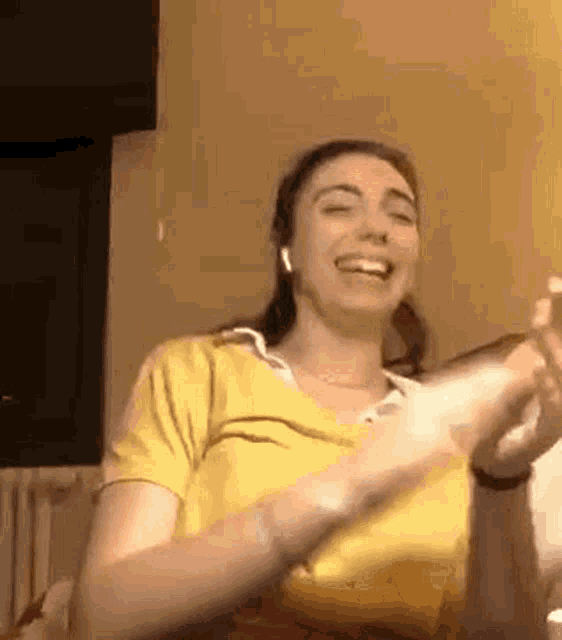 a woman in a yellow shirt is sitting on a couch with her hands in the air and smiling .