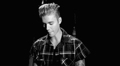 a black and white photo of justin bieber in a plaid shirt smiling .