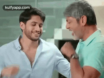 two men are standing next to each other in a room and laughing .
