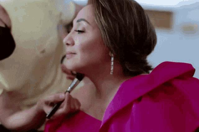 a woman in a pink dress is getting her makeup applied by a makeup artist .