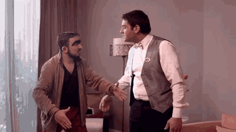 two men are standing next to each other in a room and talking .