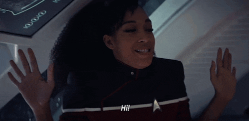 a woman in a star trek uniform is waving her hands in the air and smiling .