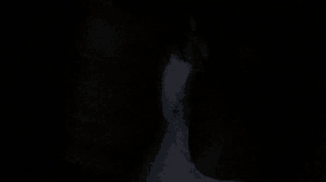 a person is standing in a dark room with a white shirt on
