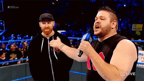 two men are standing next to each other in a wrestling ring and one is holding a microphone .