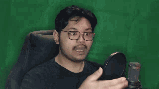 a man with glasses and a beard is sitting in front of a green screen