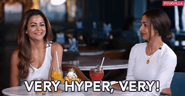 two women are sitting at a table with drinks and the words " very hyper very "