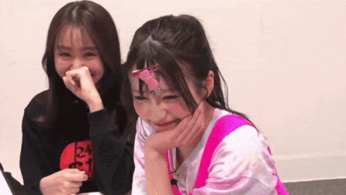 two girls are sitting next to each other laughing and one of them has a pink hair clip in her hair .