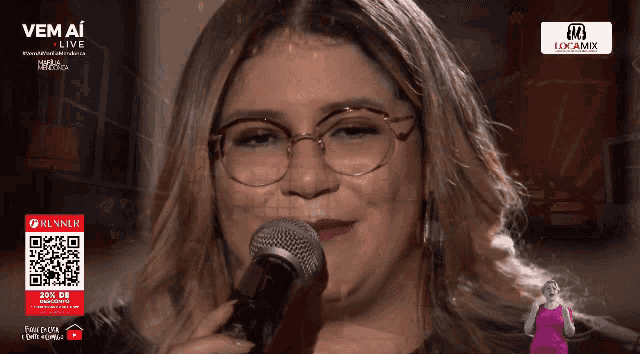 a woman wearing glasses is singing into a microphone in front of a sign that says " vem ai "